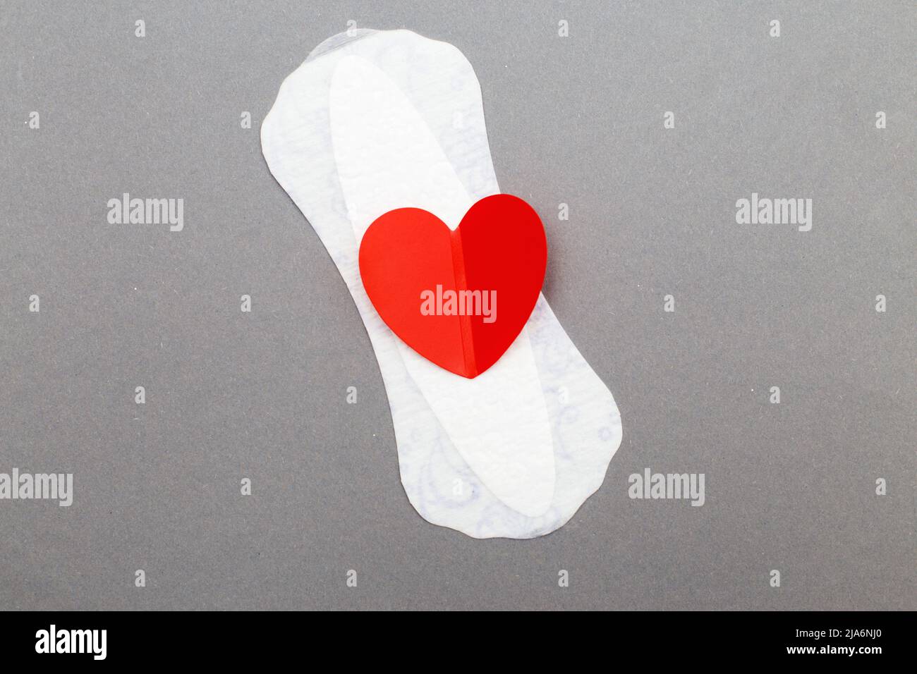 Feminine sanitary pad with a red heart on gray background. Stock Photo