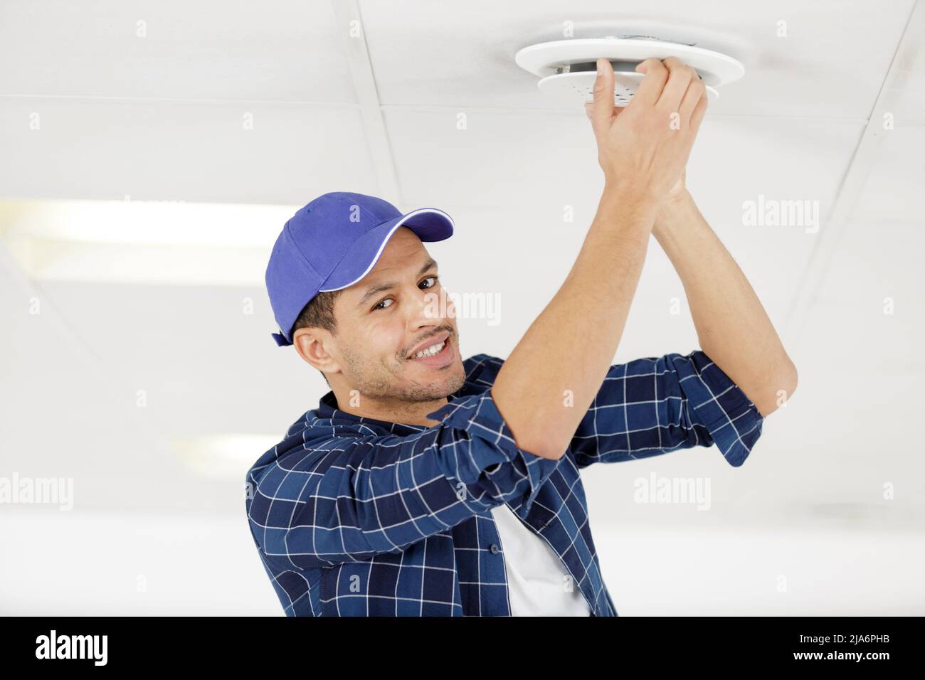 worker installing smoke detector on the ceiling Stock Photo