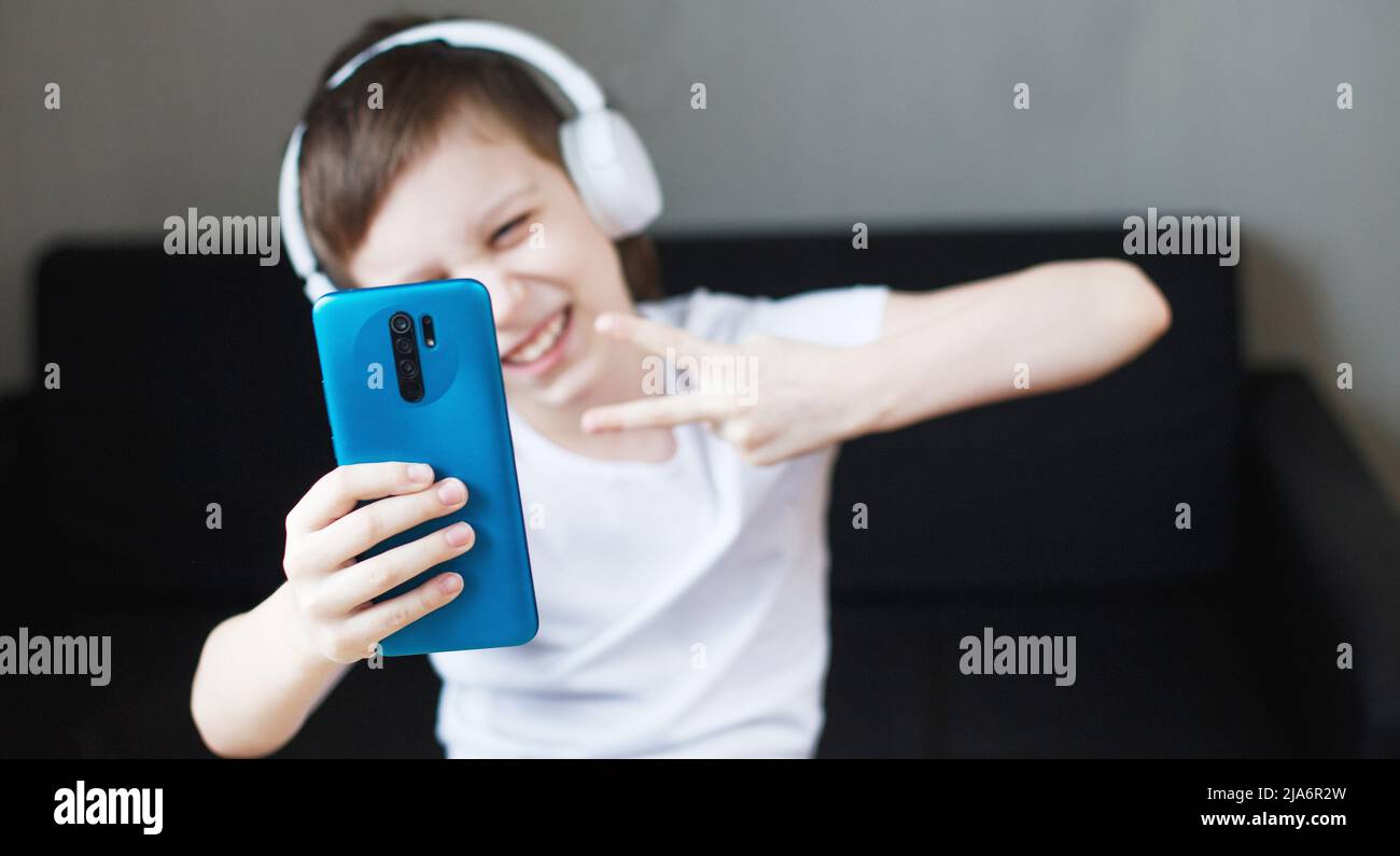 leisure, children, technology and people concept - smiling boy with smartphone and headphones having video call at home. child with mobile. banner Stock Photo