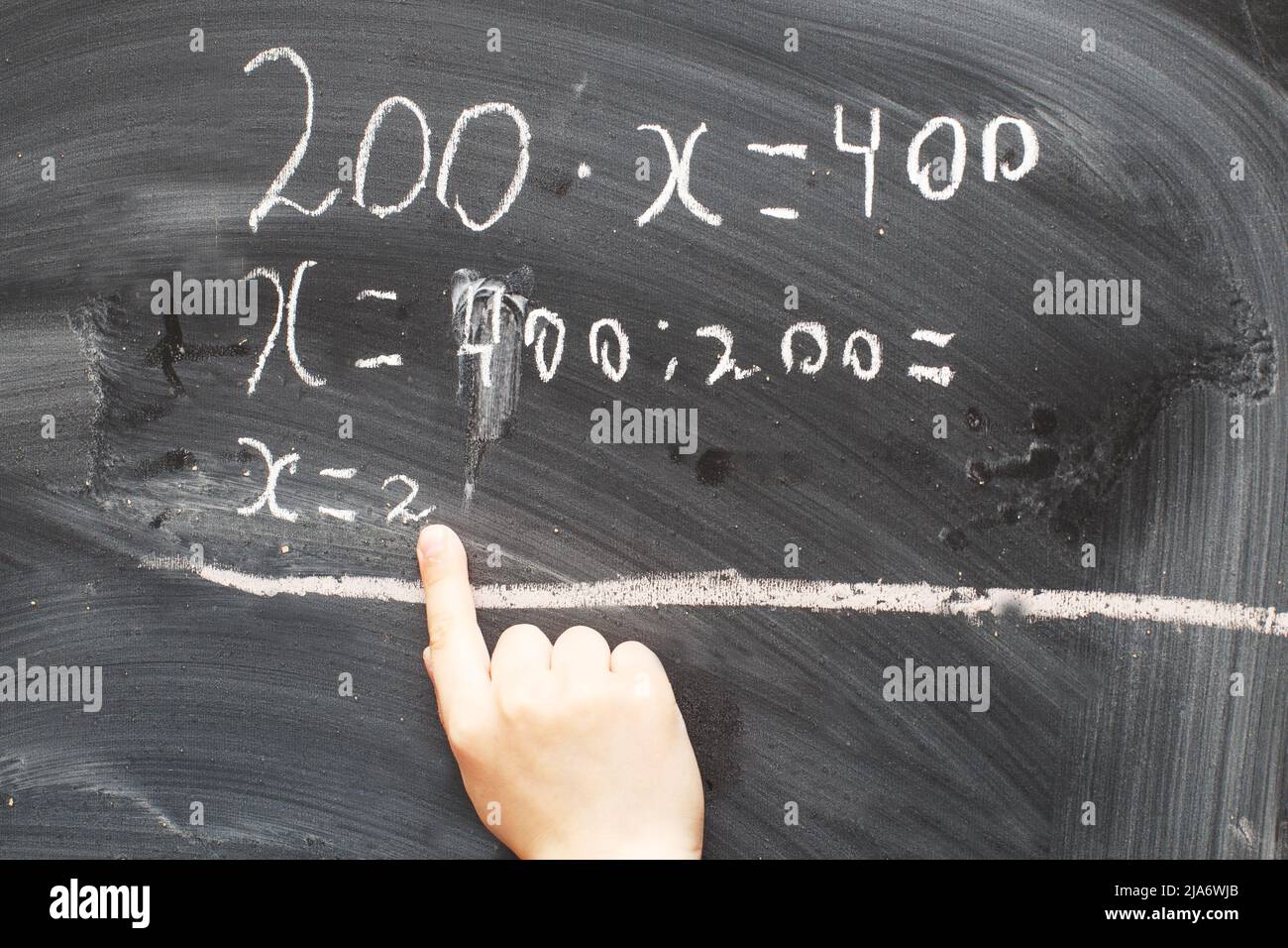 Boy standing back in front of a school blackboard and writing. Schoolboy solves math example at the chalkkboard Stock Photo