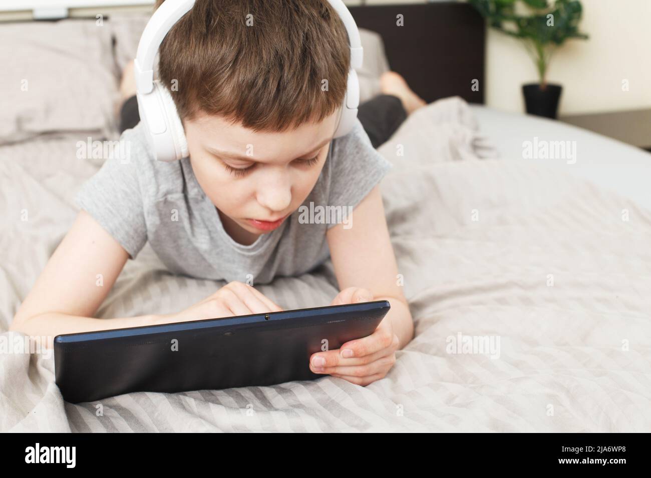 child boy lying on bed at home with pc tablet and reading online or ...