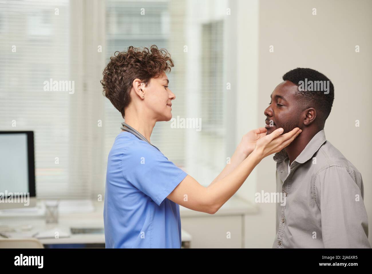 Horizontal side view shot of female doctor wearing blue uniform checking size of African American patients lymph glands Stock Photo