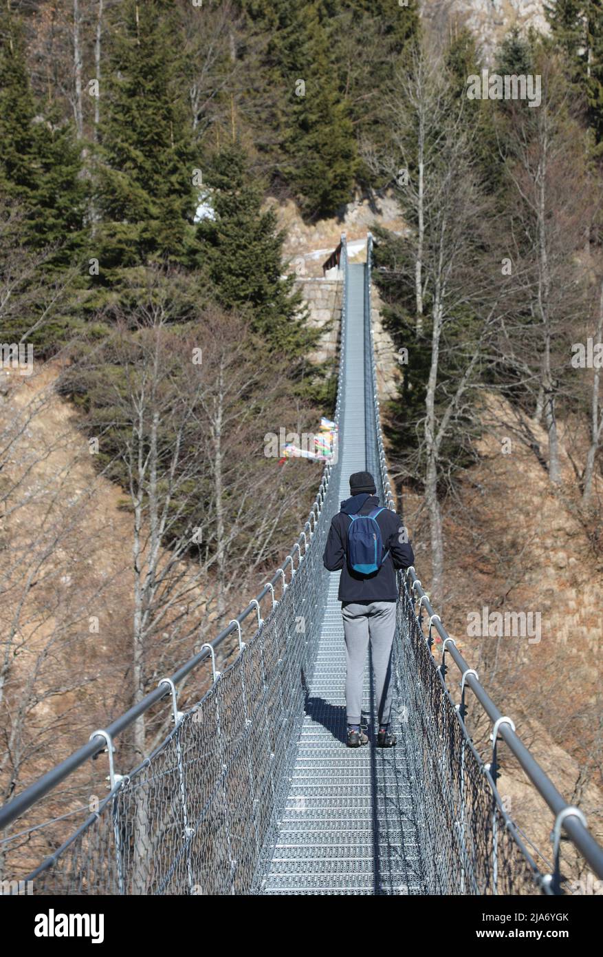 young boy walking along the suspension bridge made of sturdy steel ropes connecting the two ends of a landslide Stock Photo