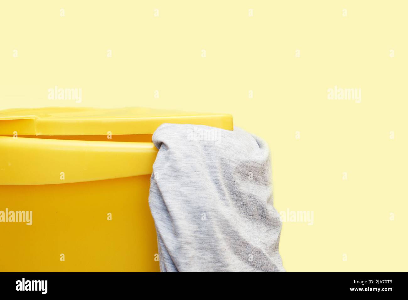 Yellow plastic laundry basket with gray clothing on a yellow background Stock Photo