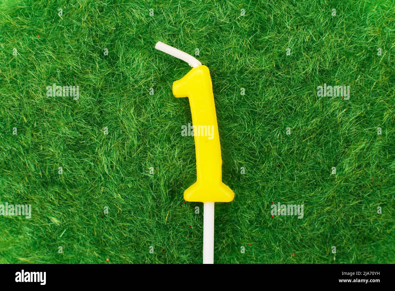 candle in the form of number one on the green grass background, a place for a greeting text Stock Photo