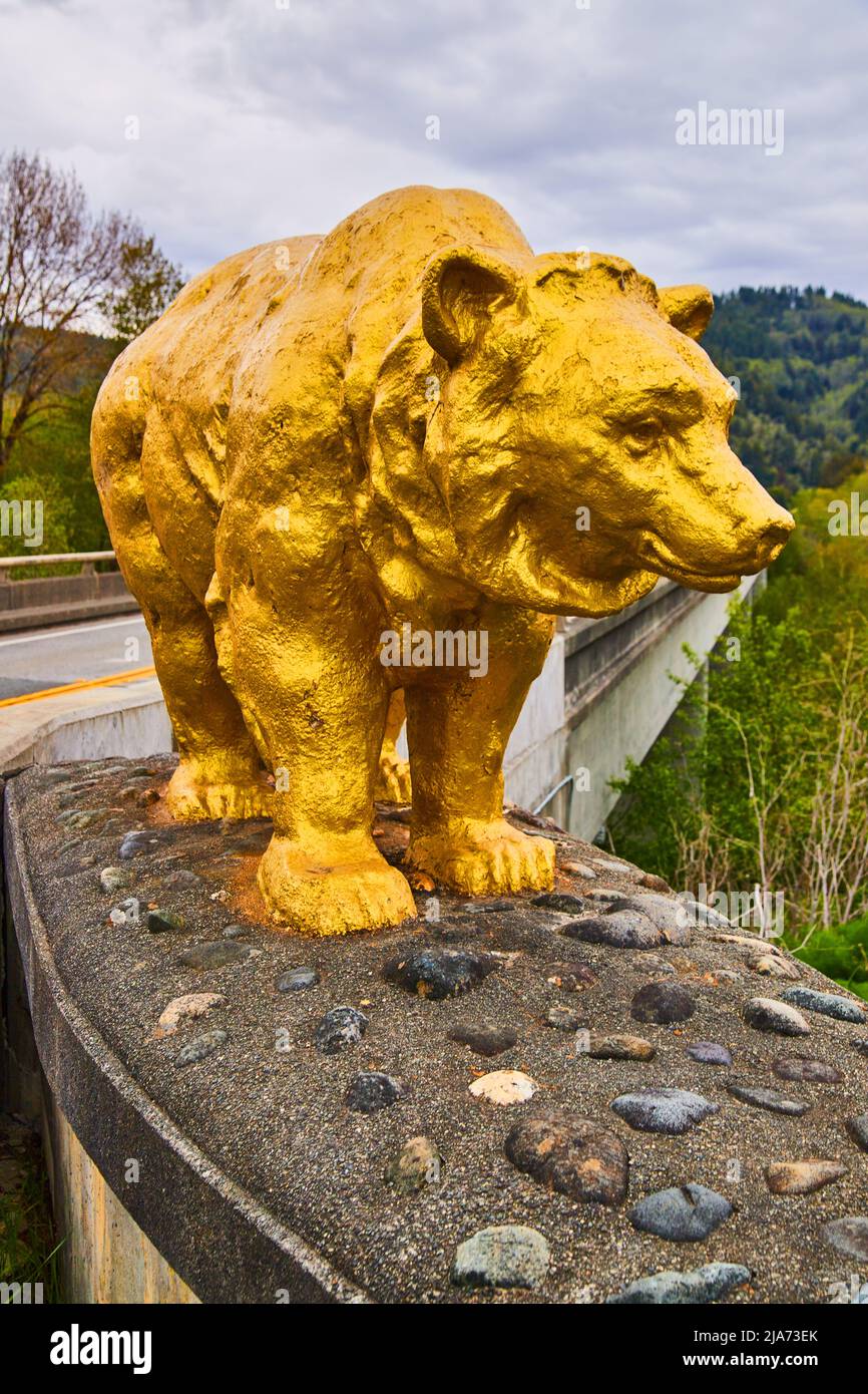 Large golden bear statue marks entrance to bridge in forest Stock Photo