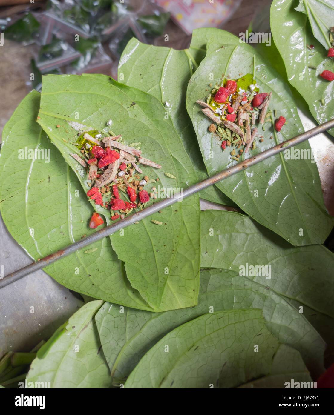 green Betel leaves or mitha paan being prepared with ingredients like areka nut or supari and other condiments in a shop for sale in india. A famous p Stock Photo