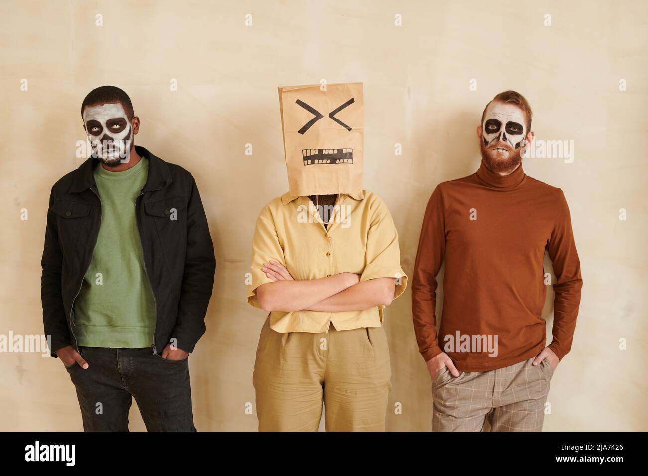 Zombie men with Halloween makeups and woman wearing paper bag with irritated face on head standing against isolated background Stock Photo