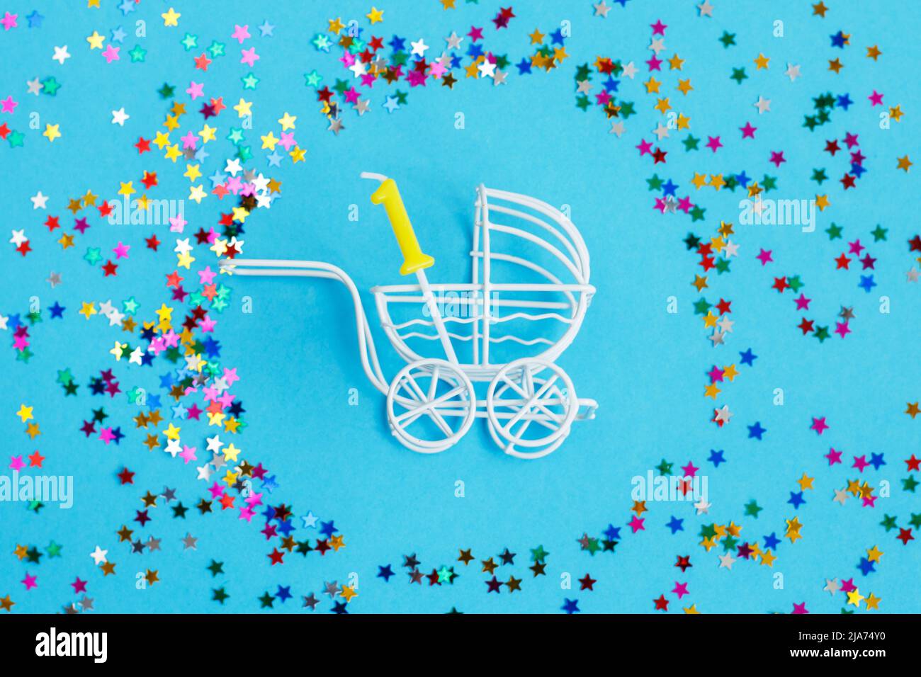 One year birthday party .baby stroller with a candle in the form of the number one on a blue background with stars confetti sequins Stock Photo
