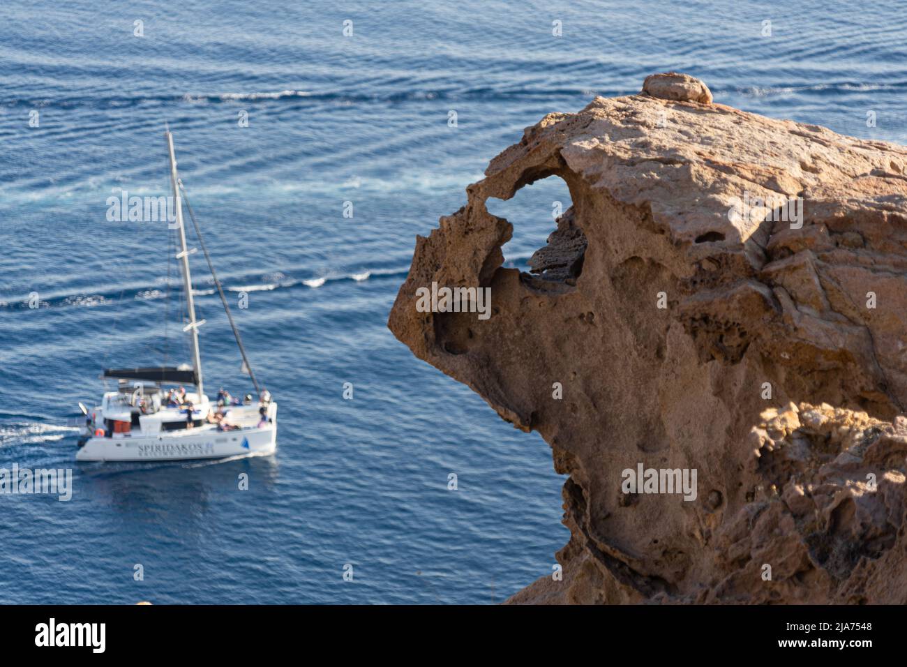 Santorini: A rocky promontory on the coast looks like a dragon's head snapping at the boats down below Stock Photo