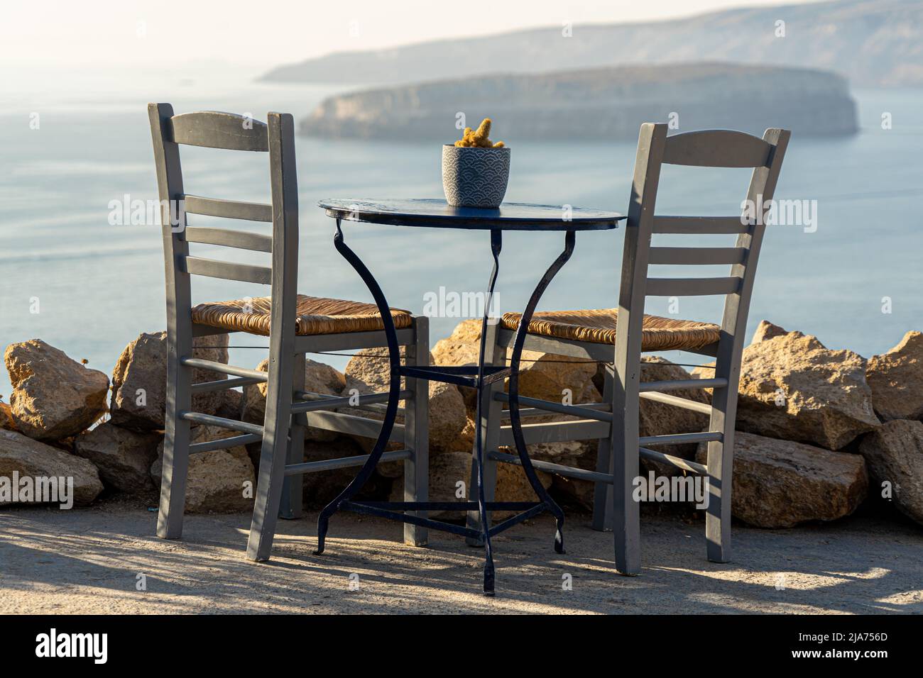 A place with a view: A single table with two chairs occupies a place with a stunning view of Santorini's caldera in the late afternoon light Stock Photo