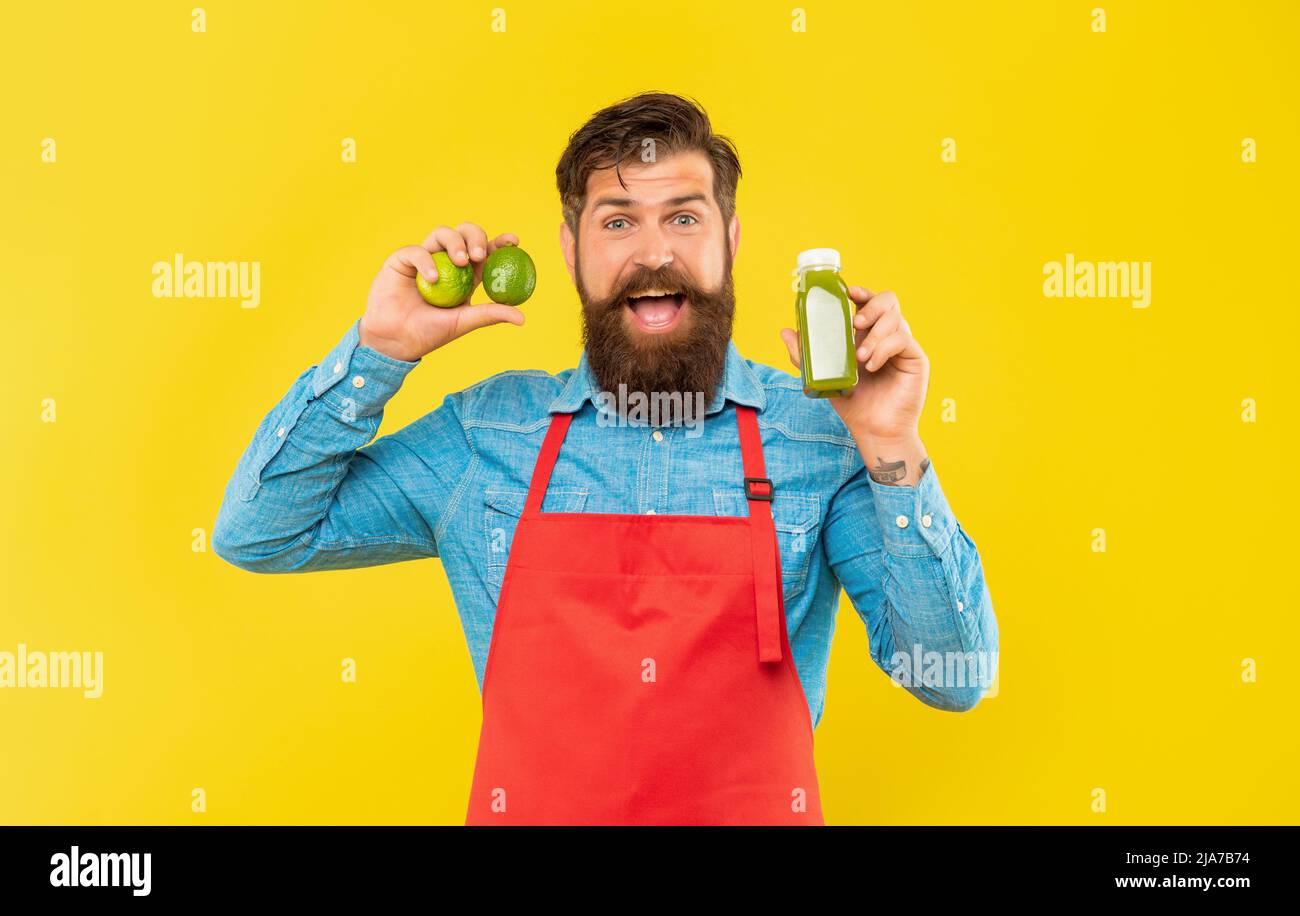Happy man in apron holding limes and juice bottle yellow background, juice barkeeper Stock Photo