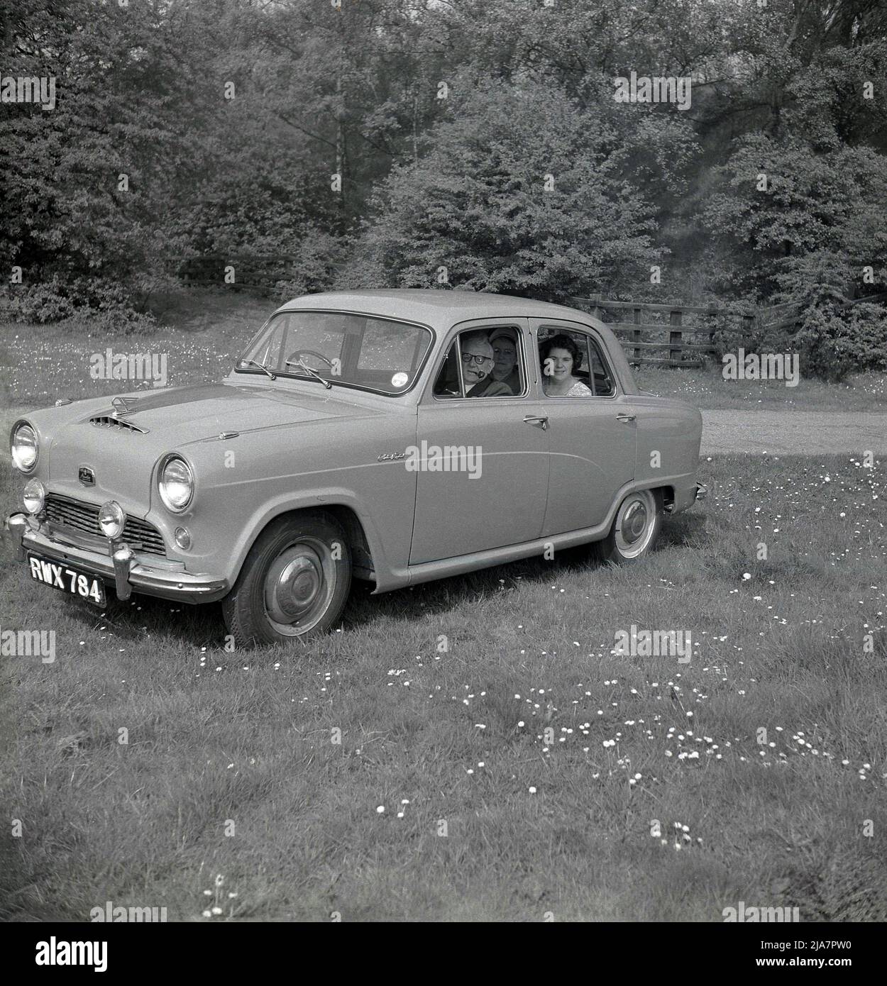 1950s, historical, post-war Britain and parked in a field at a park, a man and two ladies sitting in an Austin A40 Cambridge car of the era. The gentleman is smoking a pipe, while the two ladies sit in the back of the 4-door small family car.  In this era, going out for a day's drive to a scenic location was a popular leisure activity and is considered to be the golden age of motoring. Made by the British manufacturer, the Austin Motor Company, the Austin Cambridge motorcar was in production - with several different versions and body shapes - from 1954 to 1971. Stock Photo