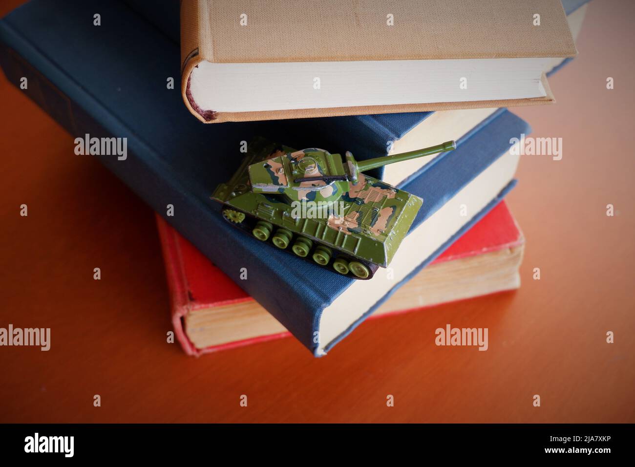 camouflage toy tank stacked on old war books on brown wooden table Stock Photo