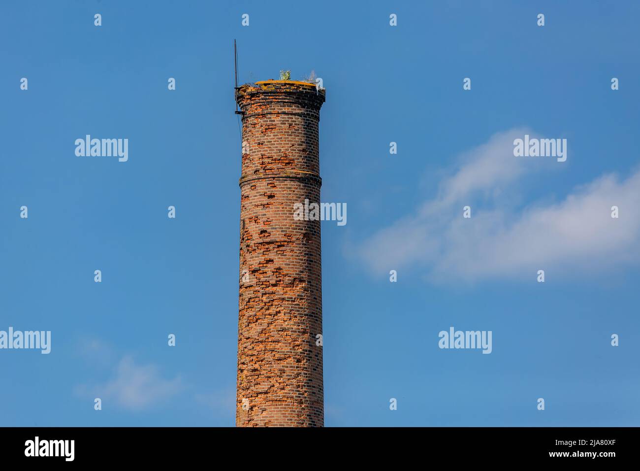 An old unused chimney made of red bricks, some of them chipped away. Sunny day with blue sky and white clouds in the background. Stock Photo