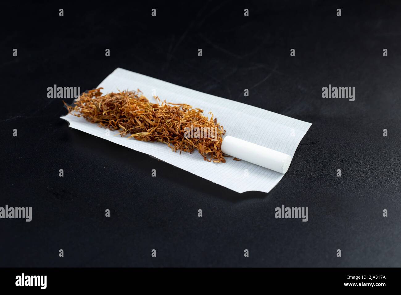 Rolling tobacco with filter tip and paper, isolated on black background Stock Photo