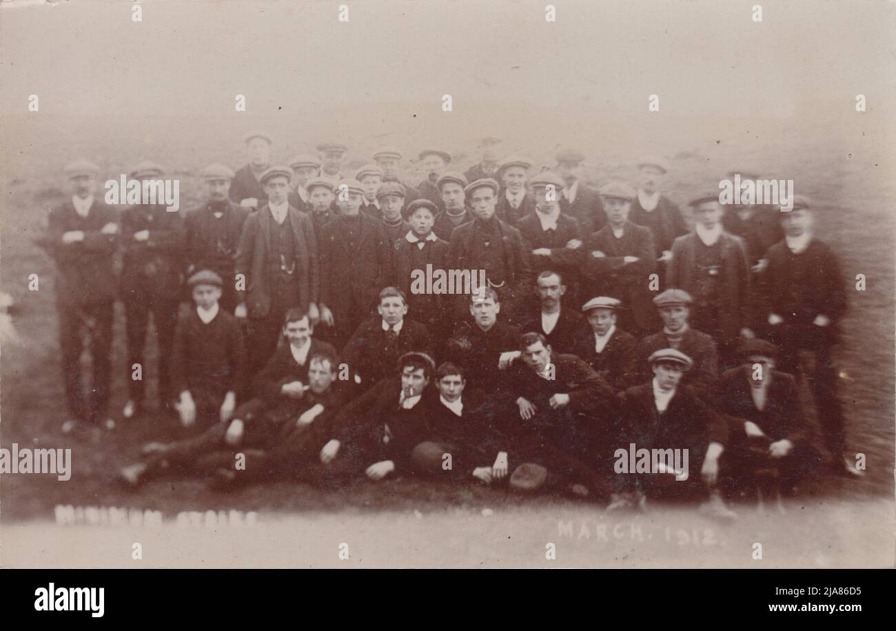 National Coal Strike, March 1912: group of men & boys, most in flat caps, standing & sitting outside in field; many of them are young. The 1912 strike was the first national strike by miners and was for the introduction of a minimum wage in the mining industry. It resulted in the passing of the Coal Mines (Minimum Wage) Act 1912, with gave miners the protection of a minimum rate of pay Stock Photo