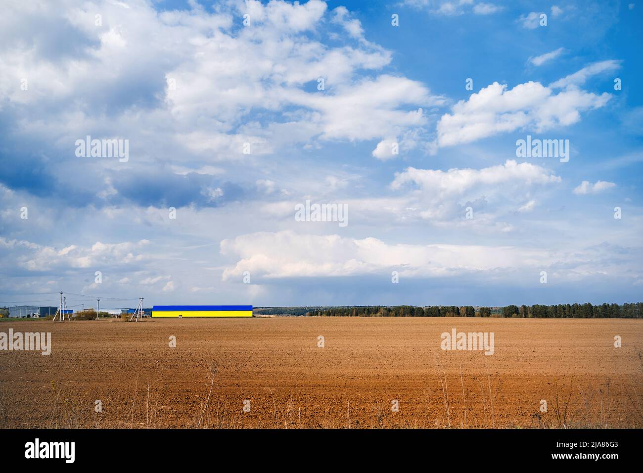 on arable land field a large hangar of yellow blue color Stock Photo