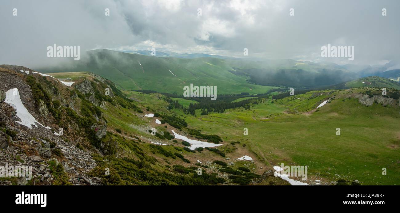 Stormy clouds and low altitude mist are covering the mountain peaks and alpine grasslands of Capatanii mountains - Carpathia. Springtime weather. Stock Photo