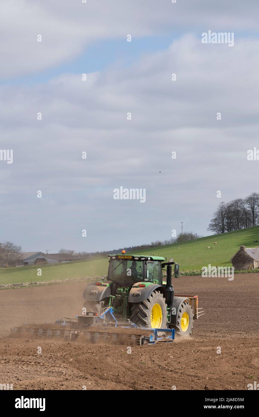 A Farmer with a Green John Deere Tractor and a Scarifier Tilling a Ploughed Field in Spring Sunshine Stock Photo
