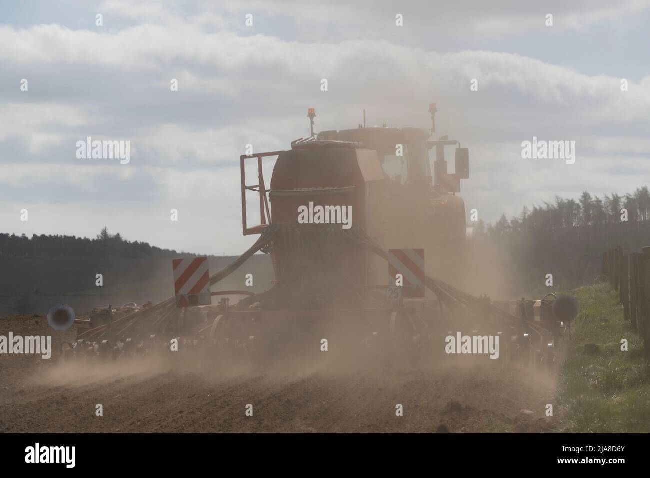 A View from the Rear of a Disc Seed Drill Operating in a Ploughed Field in Dry Weather and Creating Clouds of Dust, Backlit by Bright Sunshine Stock Photo