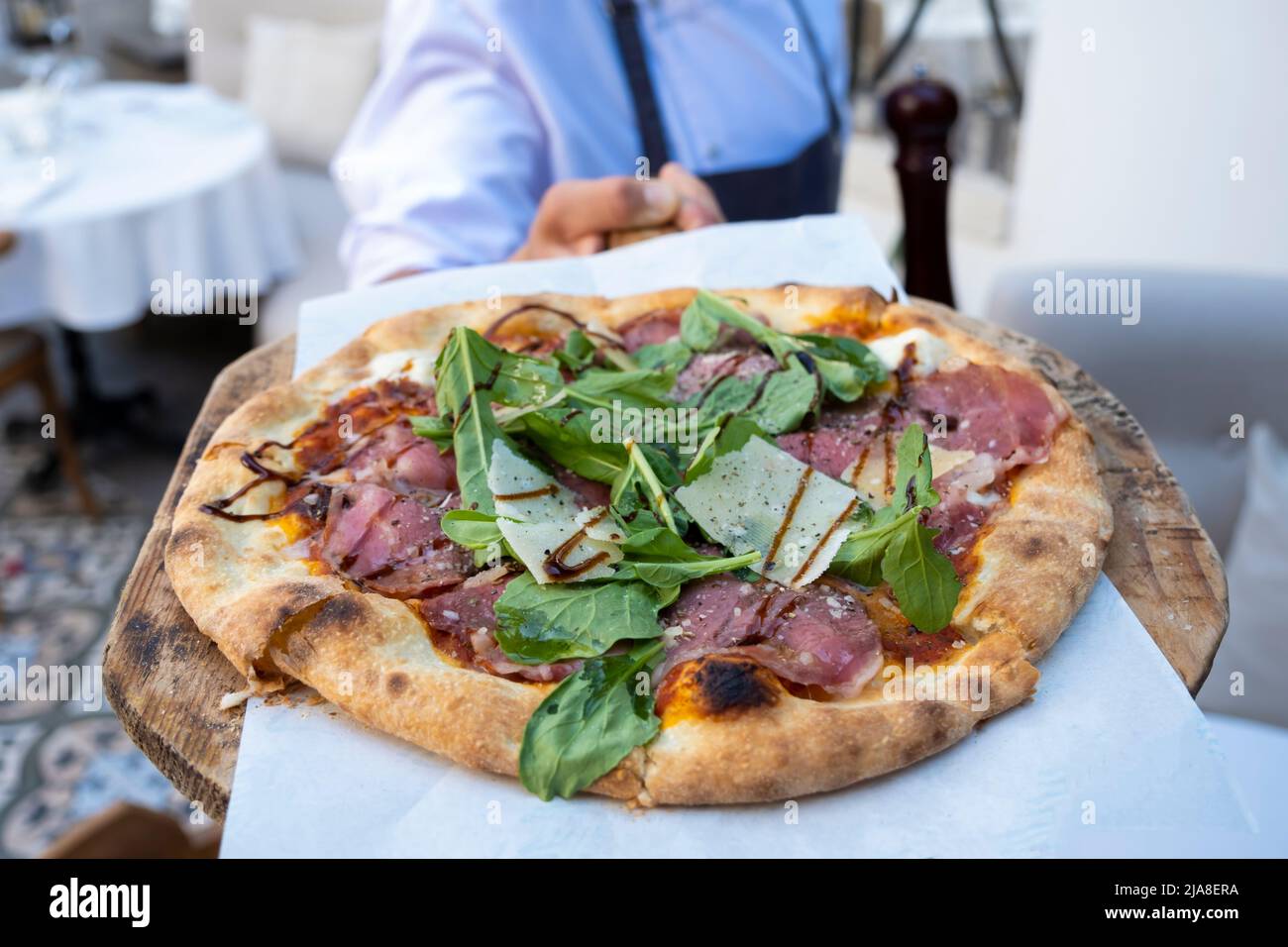 Wooden pizza plate in chef's hands and meat pizza with mozzarella cheese and arugula leaves Stock Photo