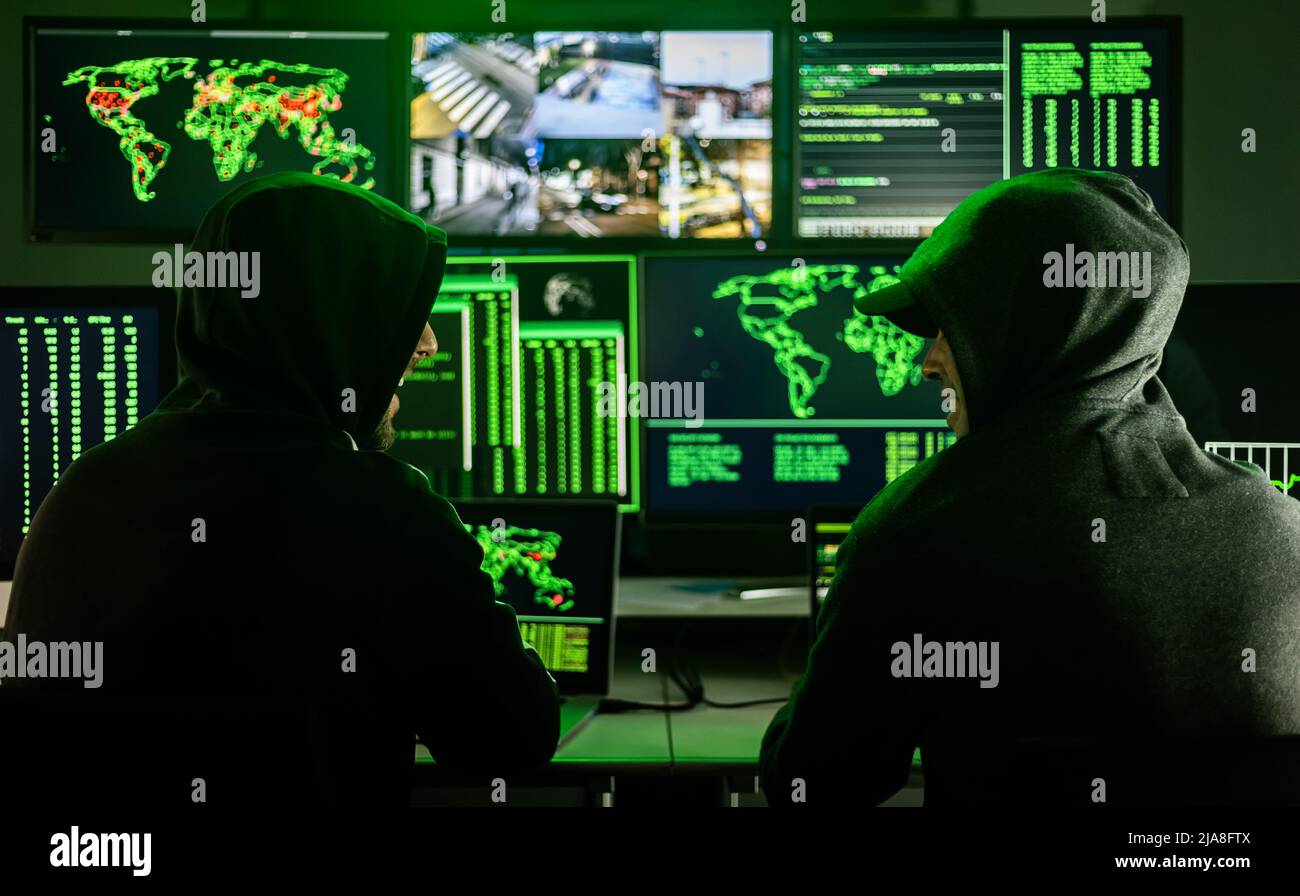 Two male hackers coding virus software in dark room Stock Photo