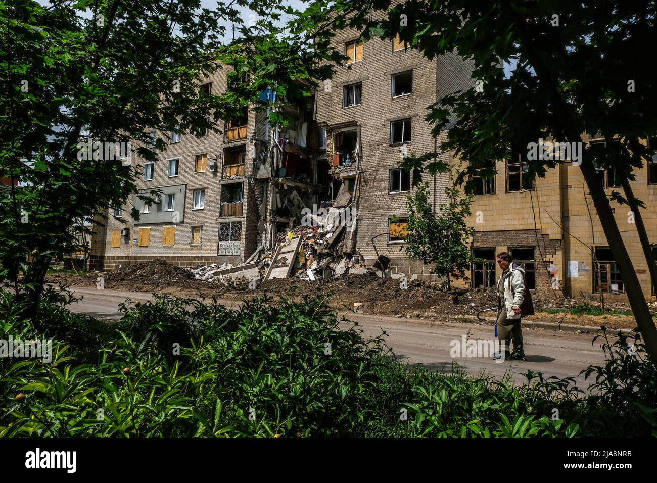 Bakhmut, Ukraine. 26th May, 2022. A woman walks past a destroyed ...