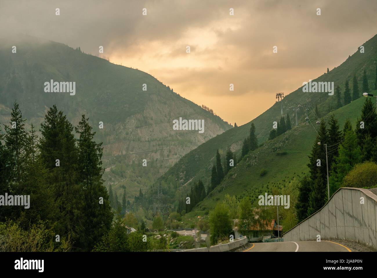 Idyllic landscape with cable car  and road  to Kazakh mountain resort 'Shymbulak' a bit foggy in sprinю Amazing  spruce forest in  of Ile-Alatau Natio Stock Photo