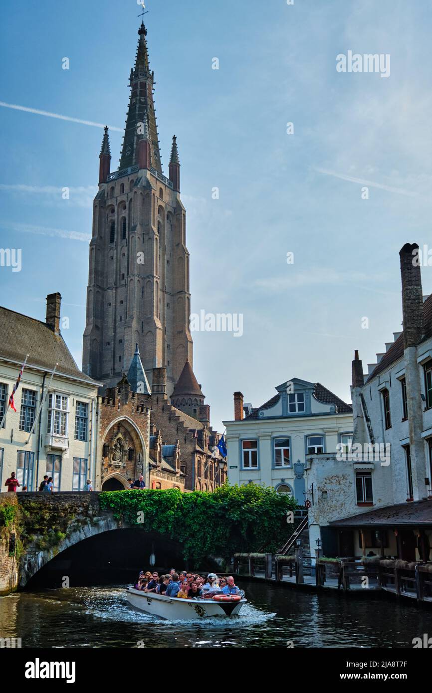 BRUGES, BELGIUM - MAY 28, 2018: Tourist boat in canal near Church of Our Lady . Brugge Bruges, Belgium Stock Photo