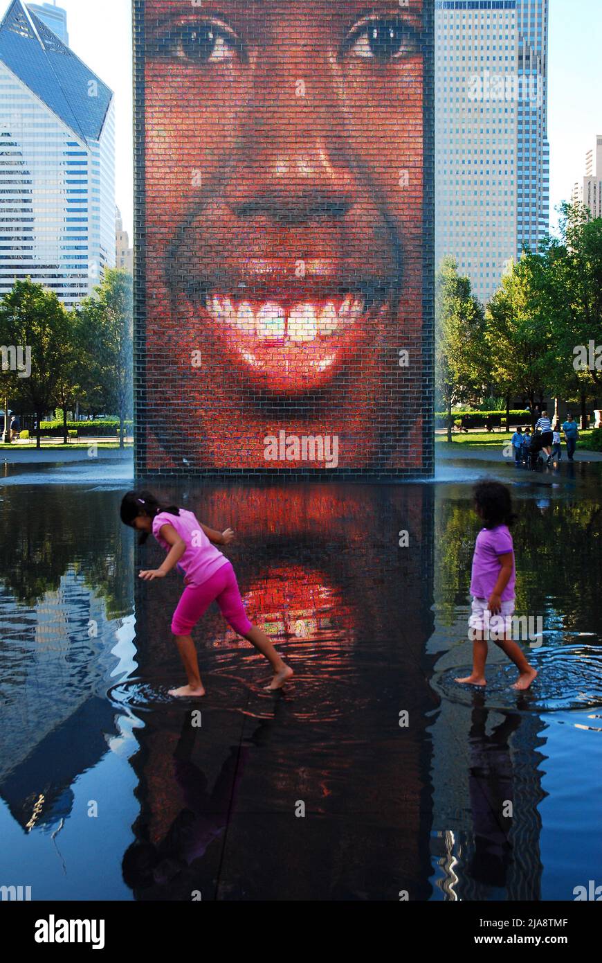 Two young girls play in the waters of the Crown Fountain in Chicago while a video display shows the different faces of the city Stock Photo