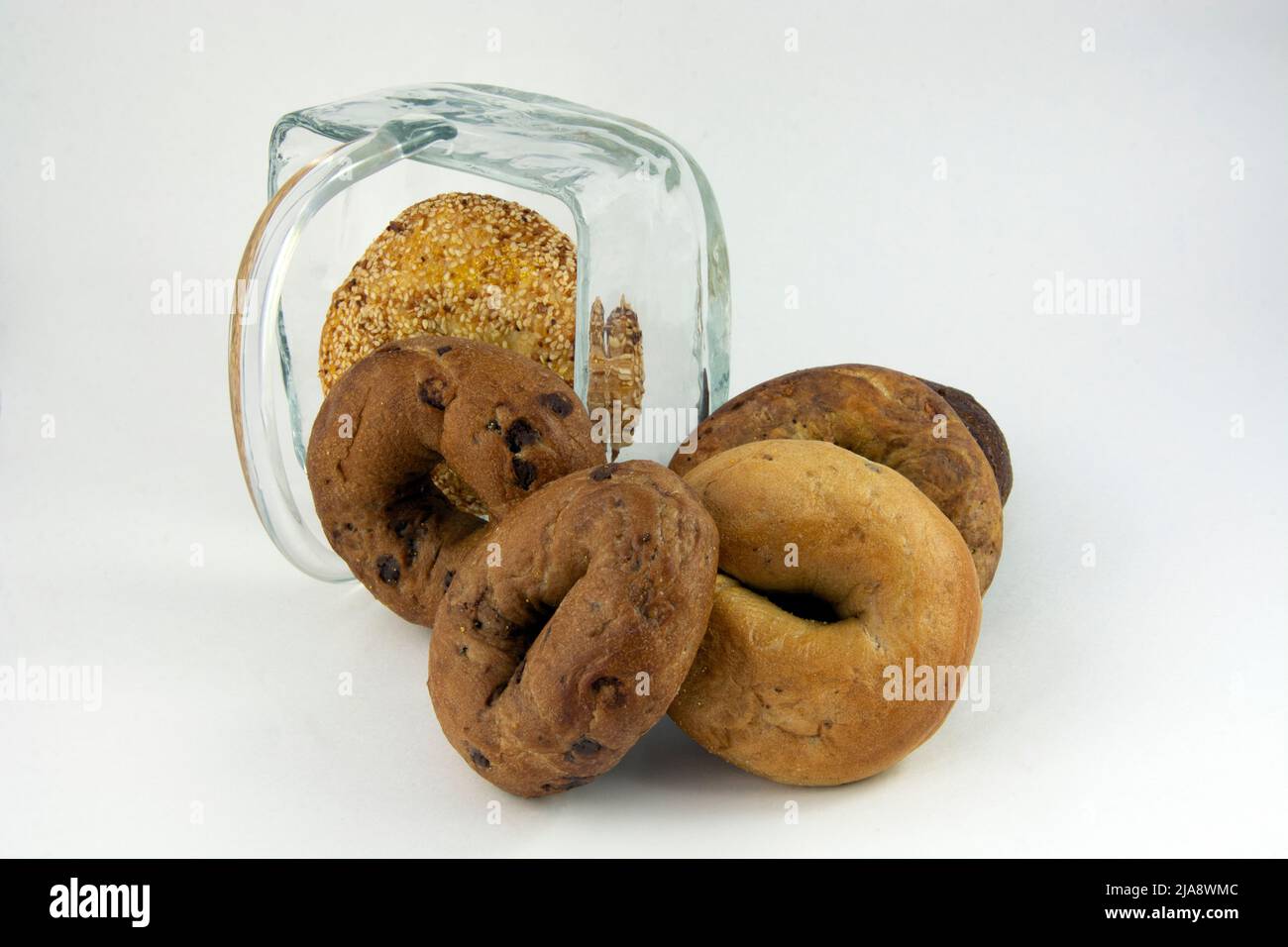 Variety of cinnamon raisin, sesame seed, and pumpernickel bagels inside and overflowing from overturned glass basket Stock Photo