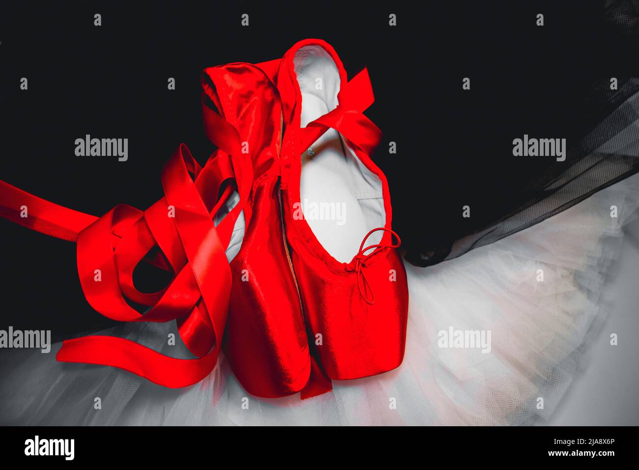 Red ballet pointe shoes resting on a white and black tutu. Stock Photo