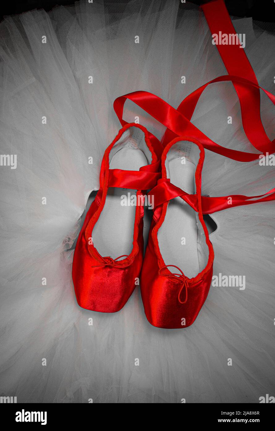 Red ballet pointe shoes resting on a black tutu. Stock Photo
