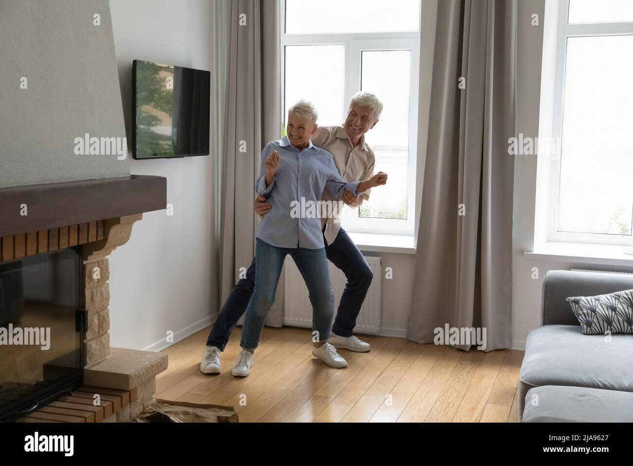 Happy energetic older age couple dancing at modern living room Stock Photo