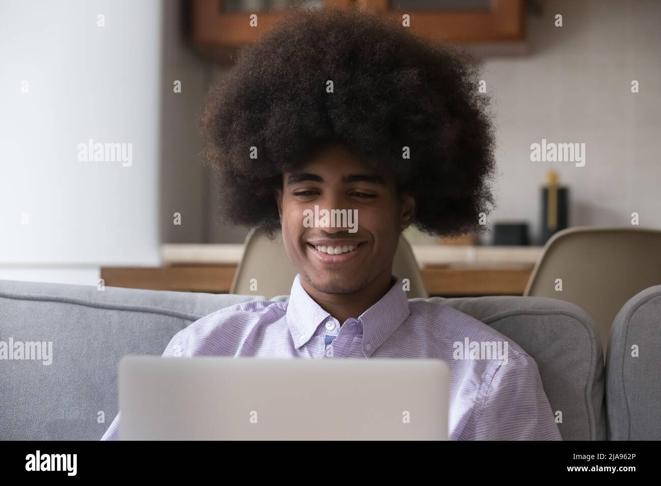 Happy cheerful Black student guy using laptop on sofa Stock Photo
