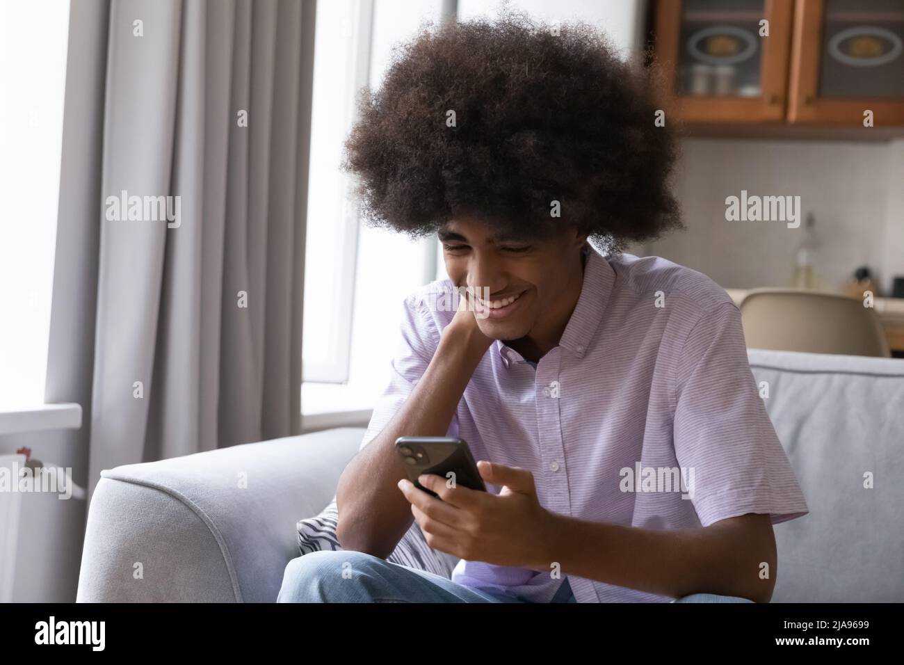 Happy teenage Black student guy typing message on smartphone Stock Photo