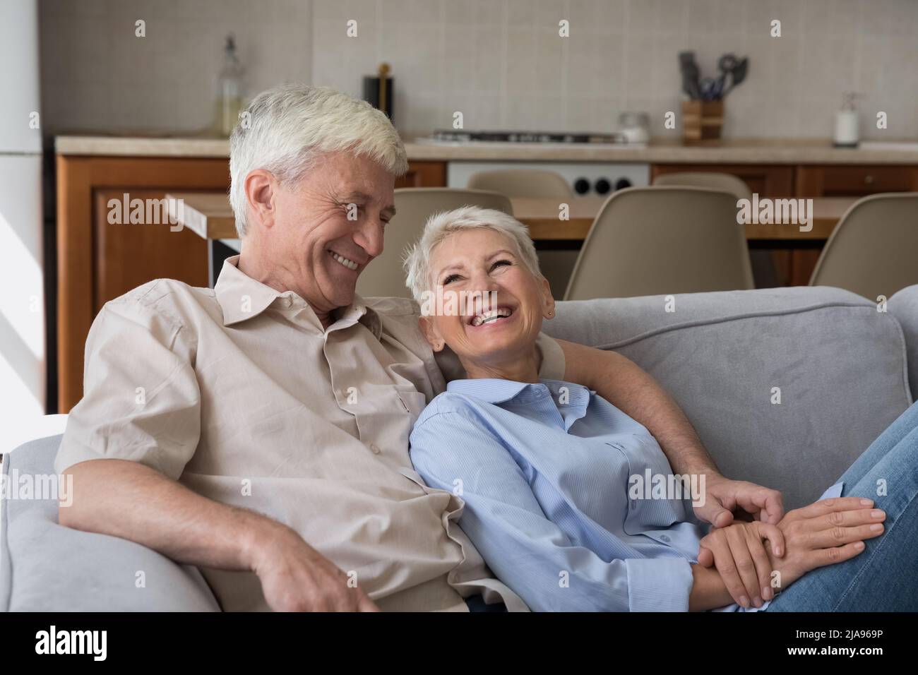 Laughing elderly spouses cuddle on couch at studio flat talk Stock