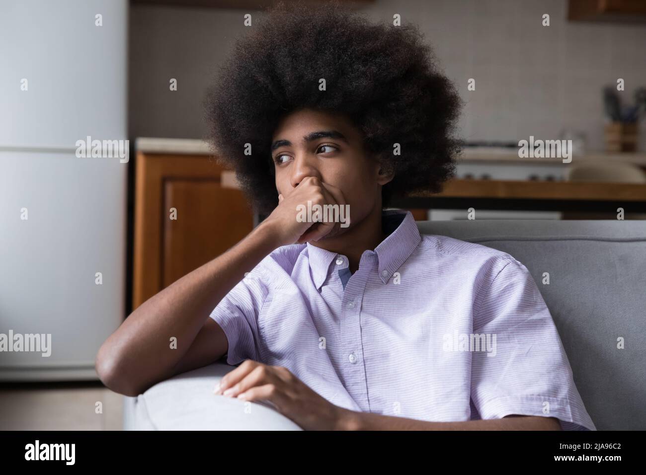 Pensive frustrated teenage African guy sitting on couch Stock Photo