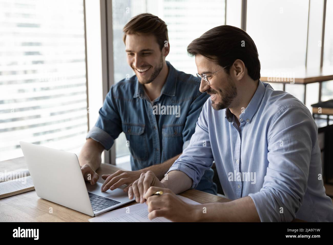 Happy startup partners using laptop and discussing project at workplace Stock Photo