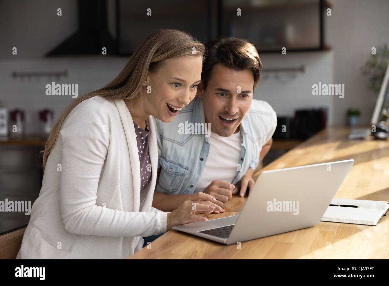 Happy surprised millennial couple using laptop, staring at screen Stock Photo