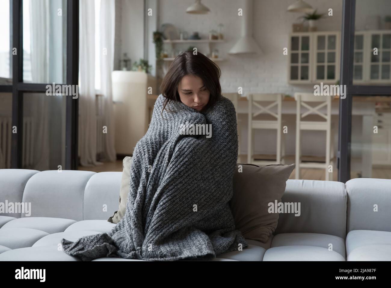 Sick unhappy girl wrapped in warm plaid suffering from cold Stock Photo