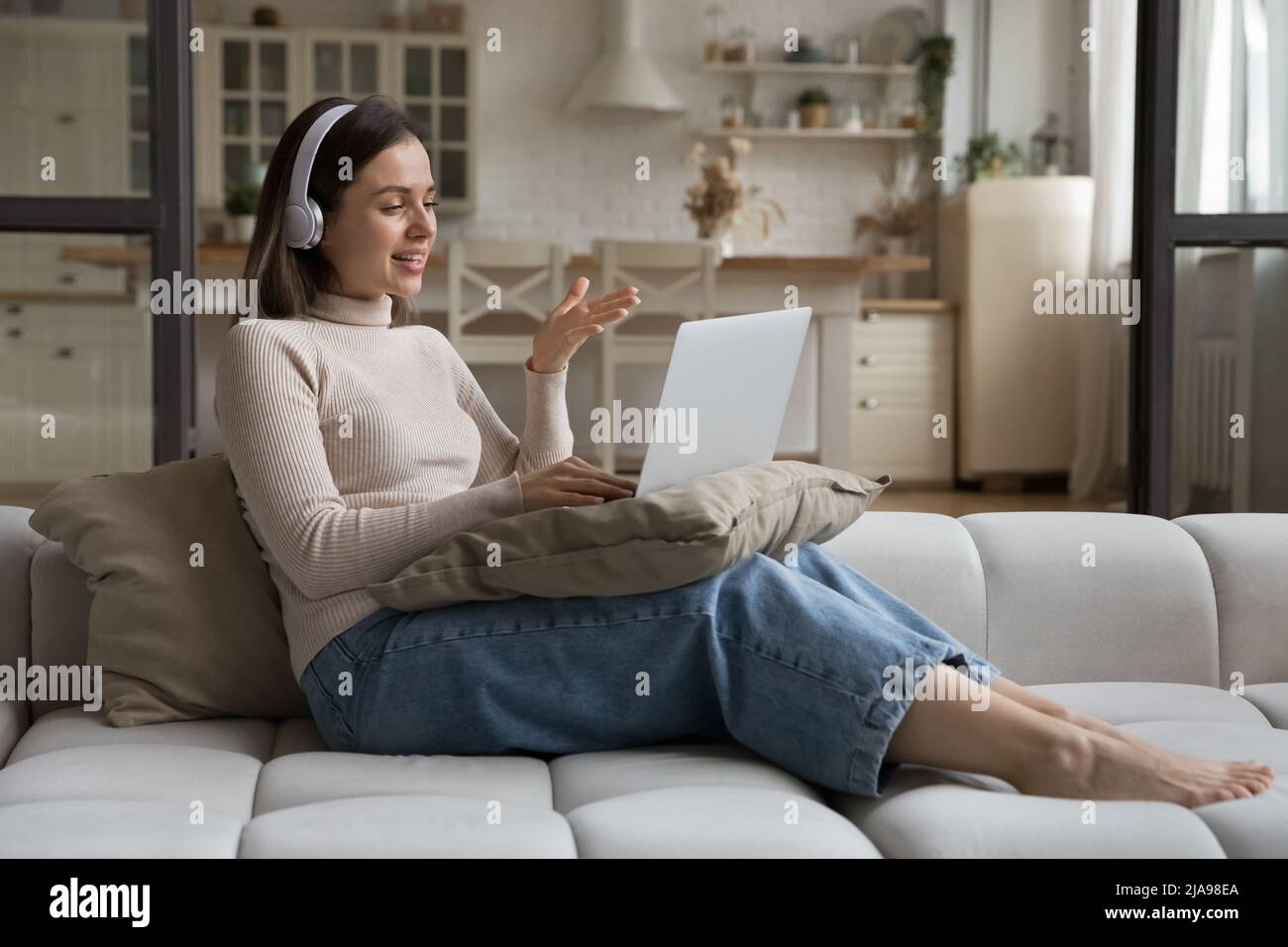 Positive freelance employee girl in headphones speaking on video call ...