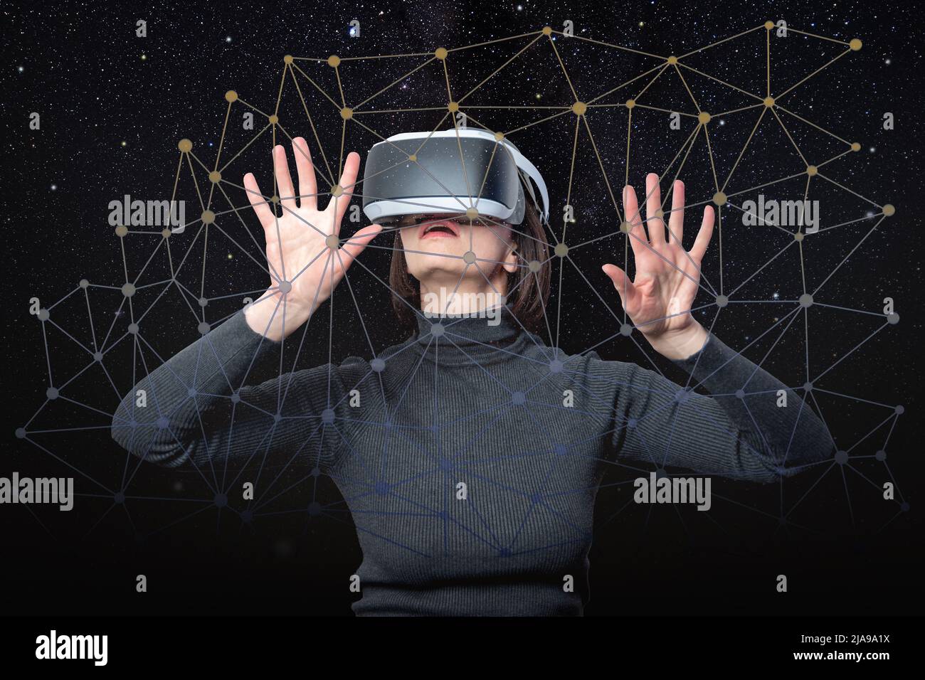 A woman in a virtual reality helmet holds her hands on a touchscreen digital screen against a black sky with stars. Virtual reality concept. Web of vi Stock Photo