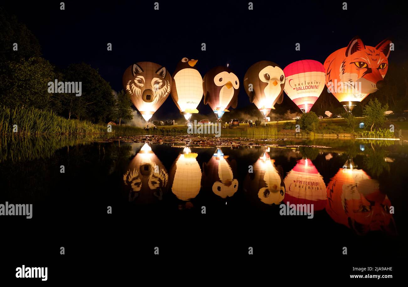 Balloons light up as they are tethered to the ground during the night
