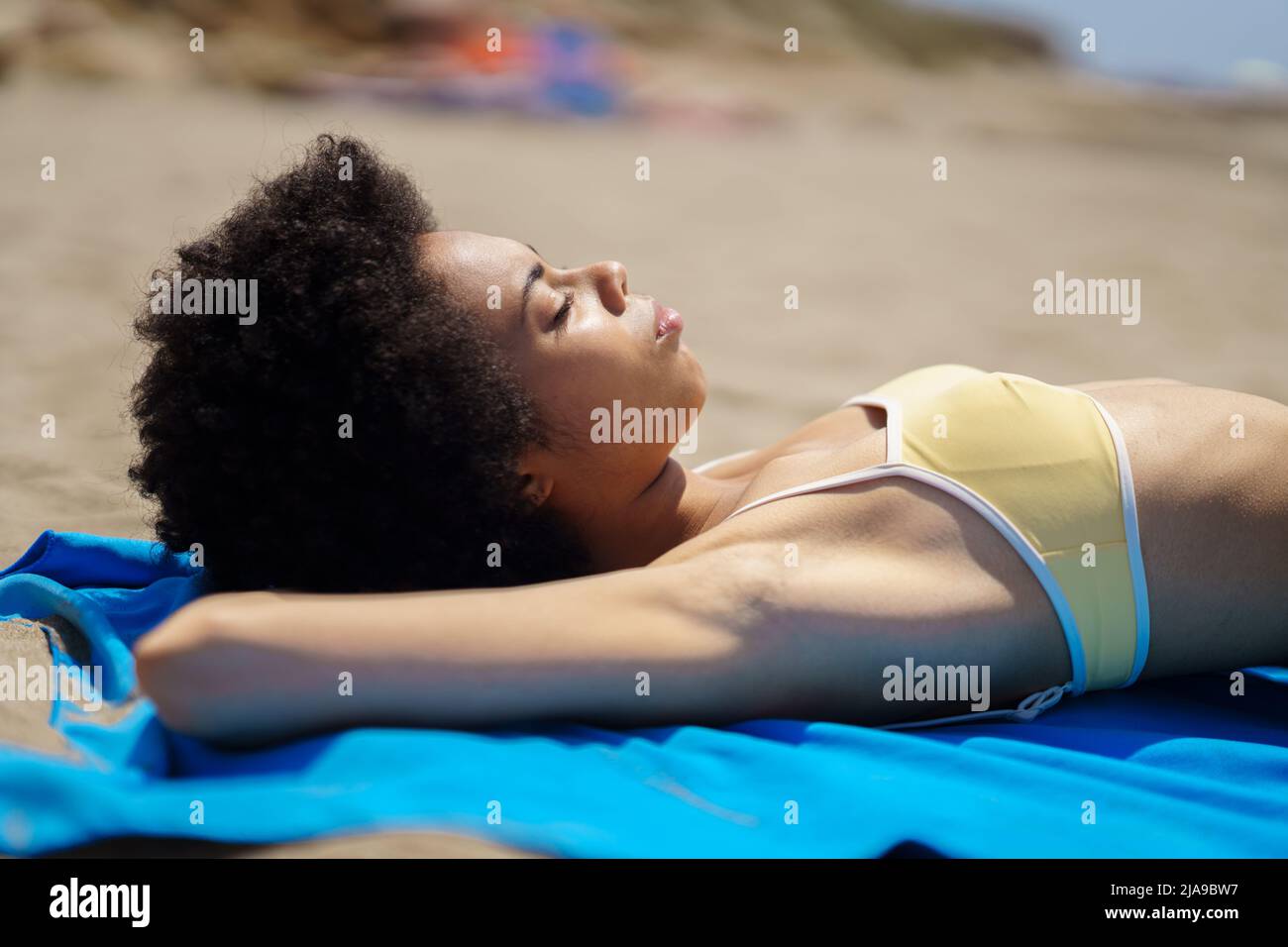 Relaxed black woman lying tanning on the sand of a tropical beach sunbathing. Stock Photo