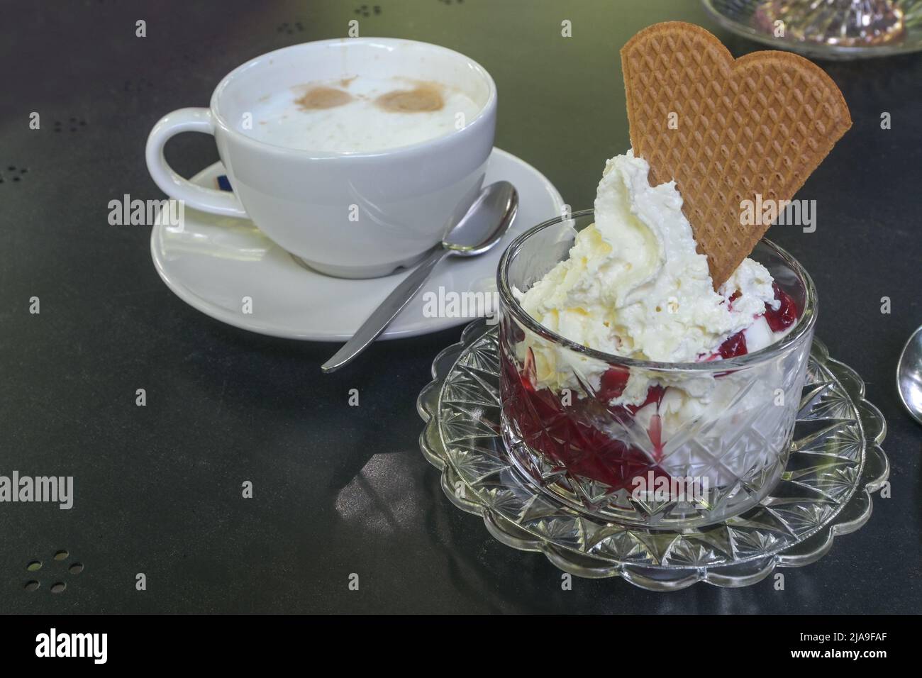 Ice cream with red fruits and whipped cream in a glass bowl and a cup of coffee on a dark table in a street cafe, copy space, selected focus, narrow d Stock Photo