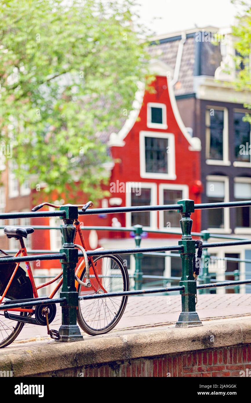 Orange dutch bicycle bike chained to bridge railings over a canal in Amsterdam with red traditional dutch house Stock Photo