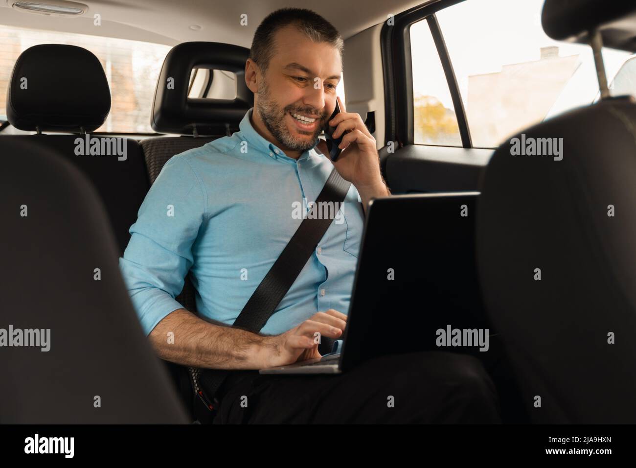 Businessman using laptop talking on smartphone while going by car Stock Photo