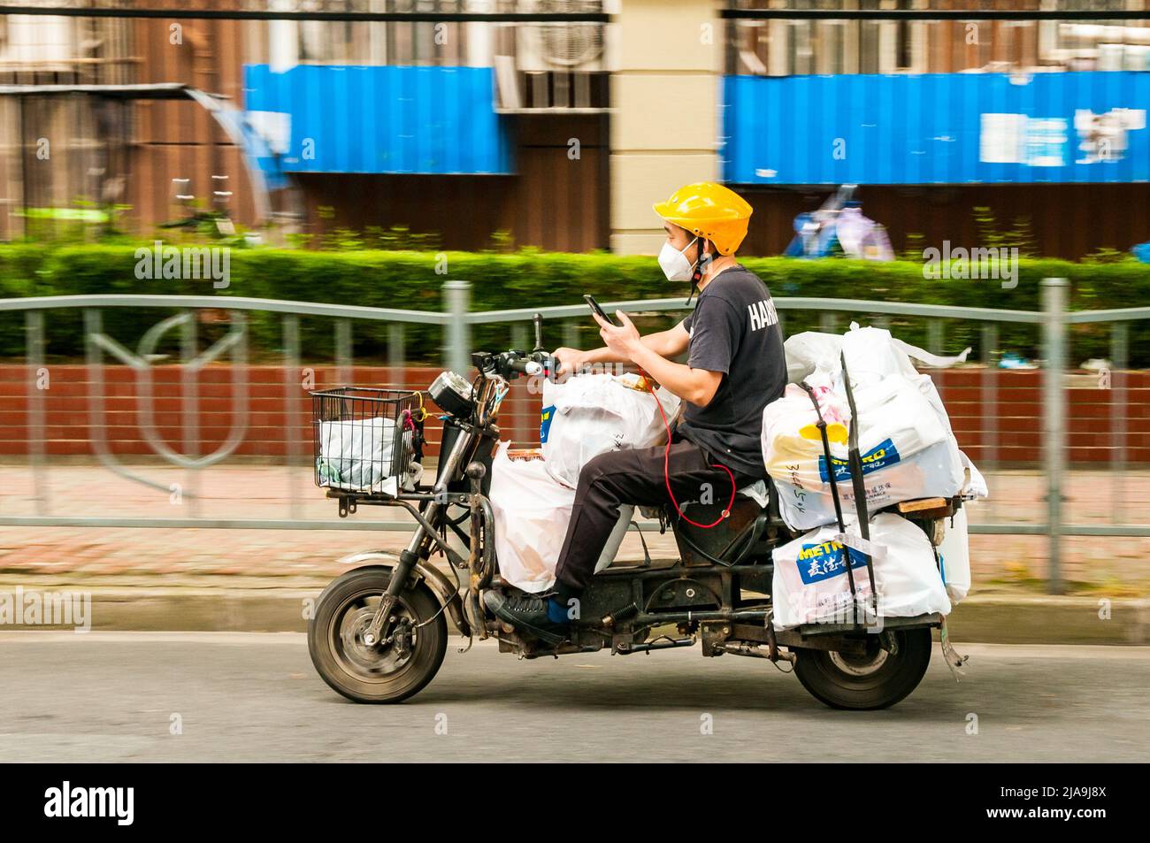 A delivery rider checks his phone while riding a scooter laden with bags from Metro supermarket in Putuo District, Shanghai, China during the end of S Stock Photo
